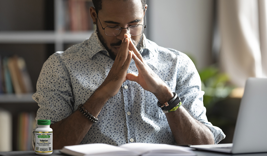 Young professional man sitting at desk with eyes closed and hands clasped