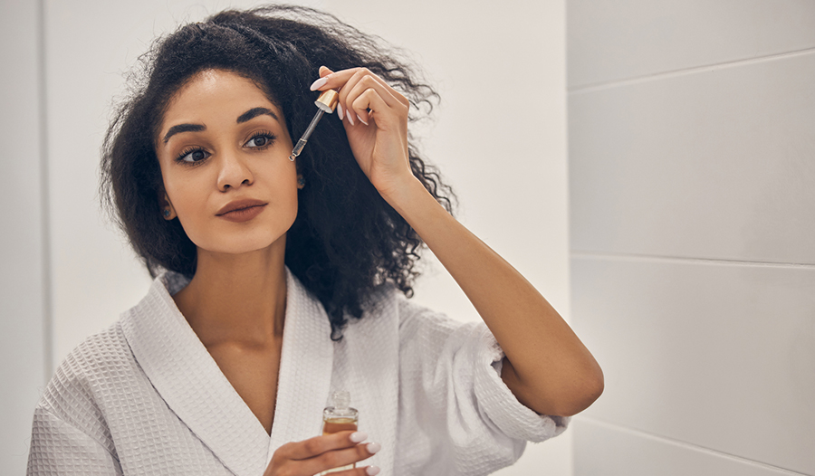 woman in white bathrobe choosing and applying serum to her face