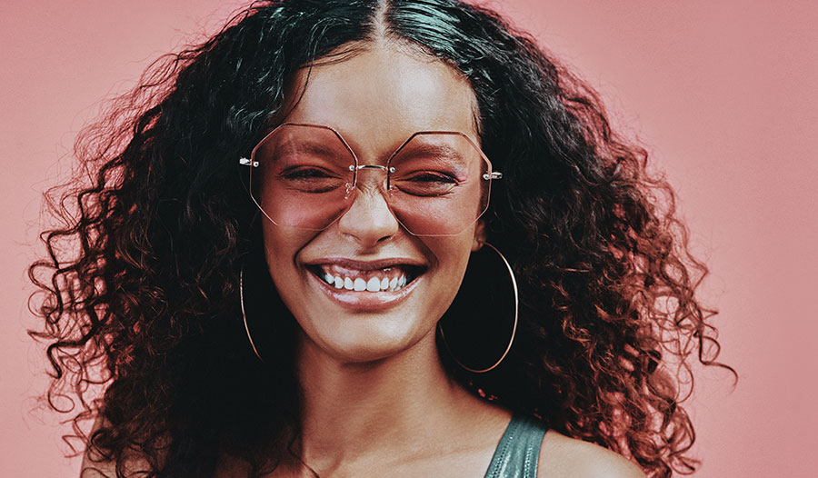 woman with glowing skin wearing fun sunglasses smiling against a pink background