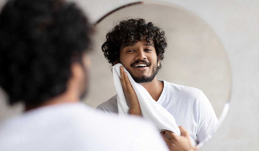 Young male washing face and looking in the mirror