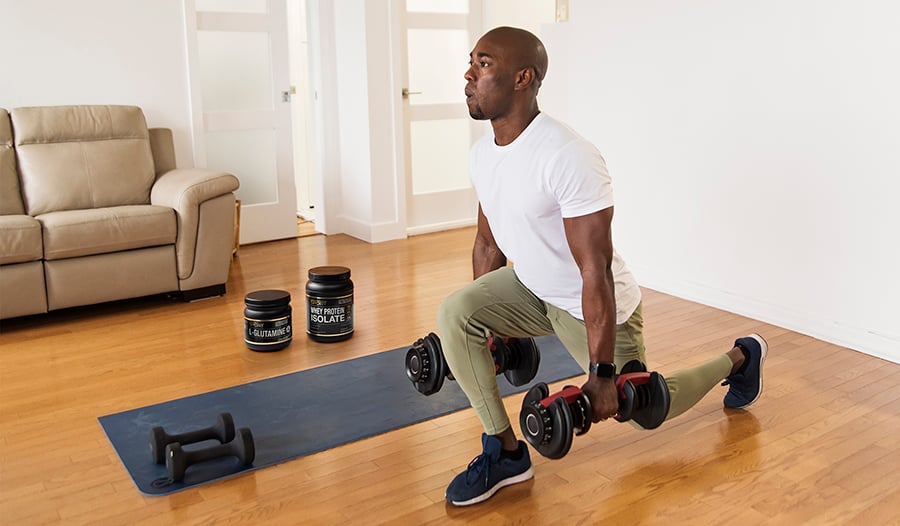 Athletic male working out at home next to yoga mat with dumbbells