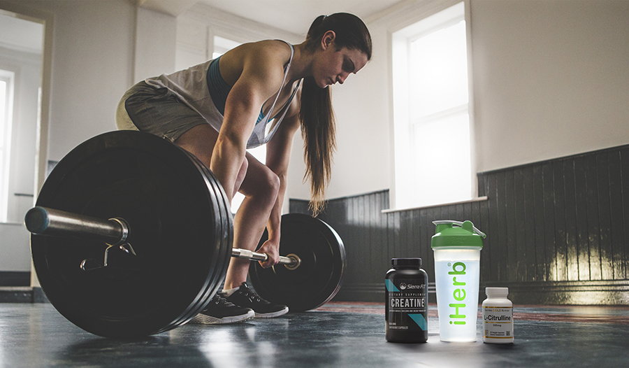 Fit woman lifting weights in the gym with sports supplements and water bottle