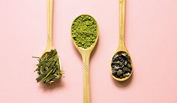 Wooden spoons of Biluochun, Matcha (powdered green tea) and Longjing on a pink background