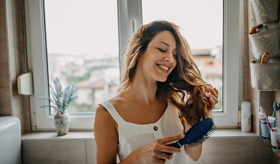 Young woman brushing her hair in bathroom by the window