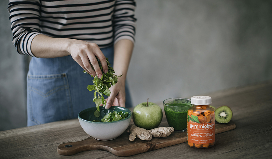 Woman making green smoothie with turmeric supplements on table