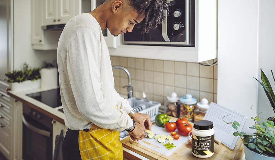 Man wearing apron cutting vegetables in kitchen with shake powder on counter