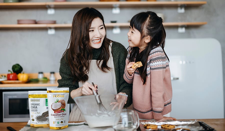 Asian mother and daughter baking in kitchen with coconut chips and chia seeds