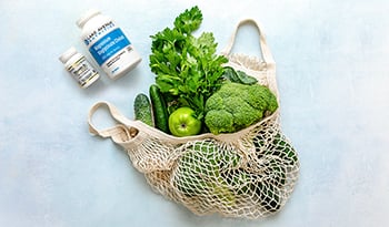Green vegetables in reusable bag on table with supplements