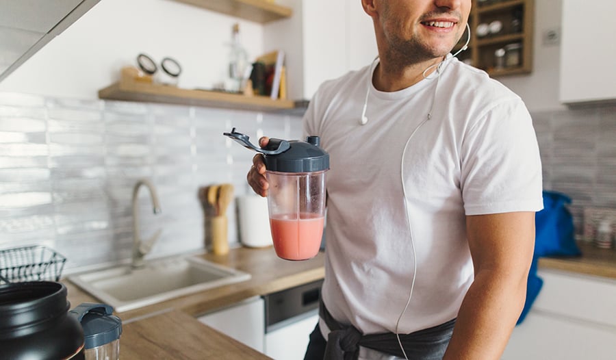 Athletic young male drinking a sports drink in the kitchen
