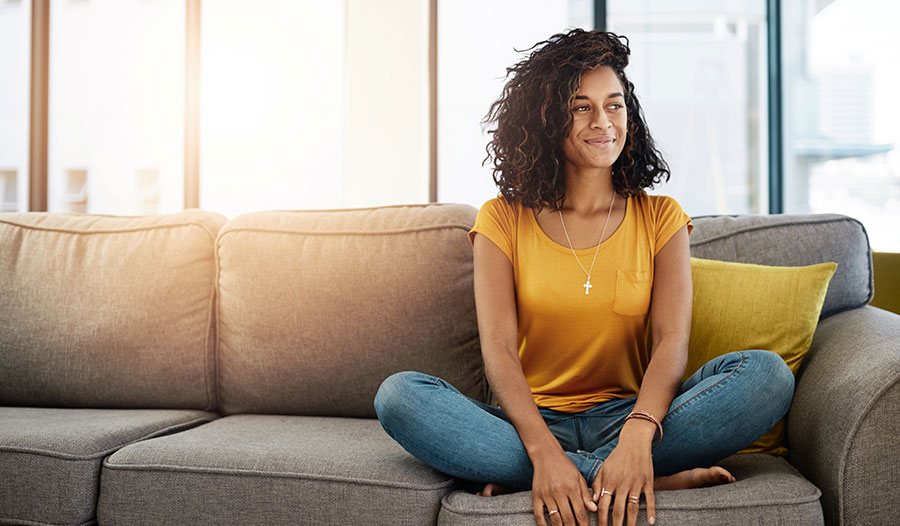 woman sitting on her couch listening to her body and smiling