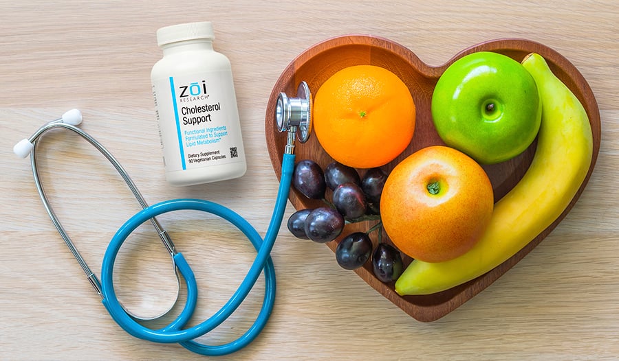 Fruit in heart shaped bowl, stethoscope, and cholesterol support supplement on wood table