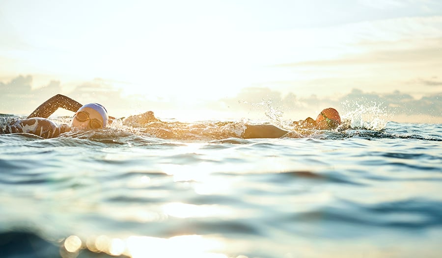 Healthy women swimming in the ocean wearing swim caps and wet suits