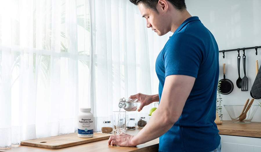 Fit male pouring glass of water with magnesium supplement bottle on counter