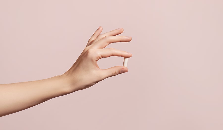 Hand holding a supplement on pink background