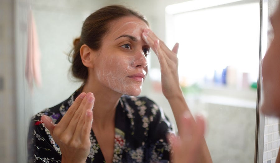 woman washing face with cleanser to treat malassezia overgrowth