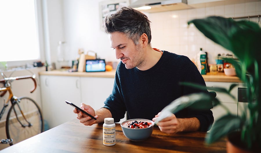 Male eating breakfast in kitchen looking at his phone