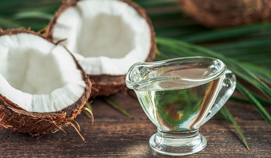 Coconut oil in glass on wooden table with coconuts and palm leaves