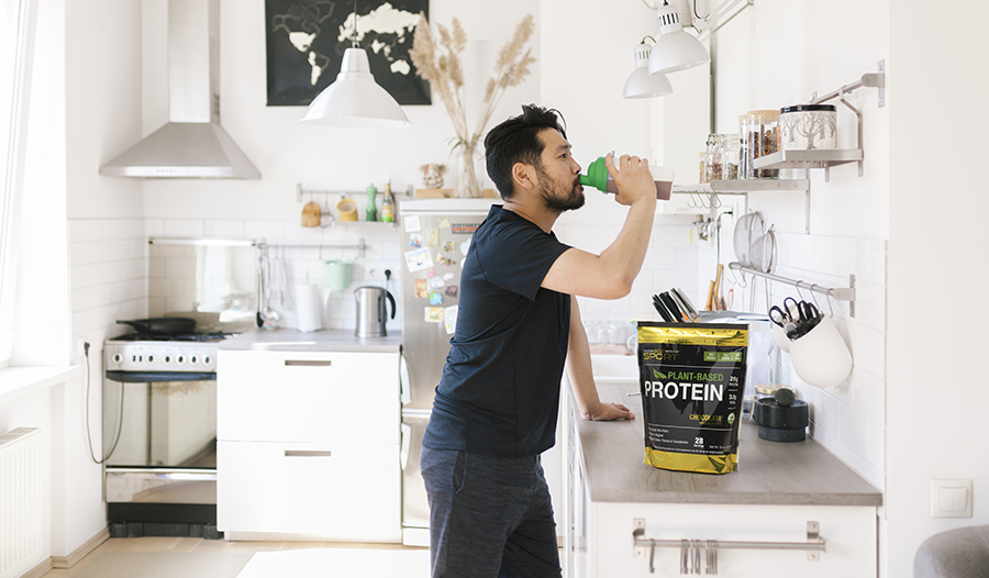 Asian man drinking protein shake in kitchen