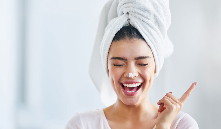 woman smiling with eyes closed and hair up in a towel with a dab of collagen cream on her nose