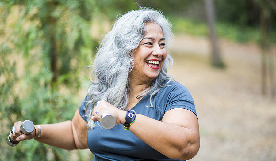 Healthy happy mature woman exercising outside with light weights 