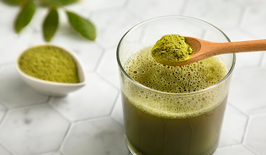Moringa powder in wooden spoon and glass of water