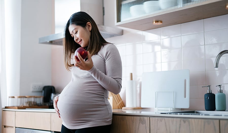 Pregnant woman smiling eating an apple in the kitchen