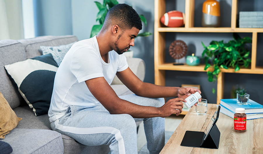 Male looking up supplement ingredients in living room with multivitamin on table