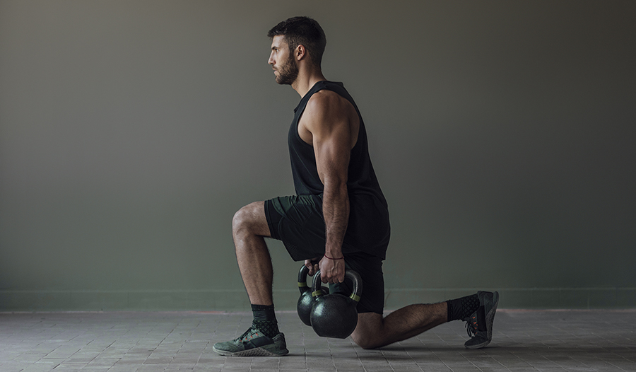 Muscular athlete doing lunges with kettlebell weights, strength training