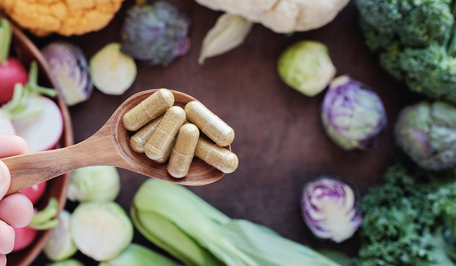 Supplements in wooden spoon over cutting board with vegetables