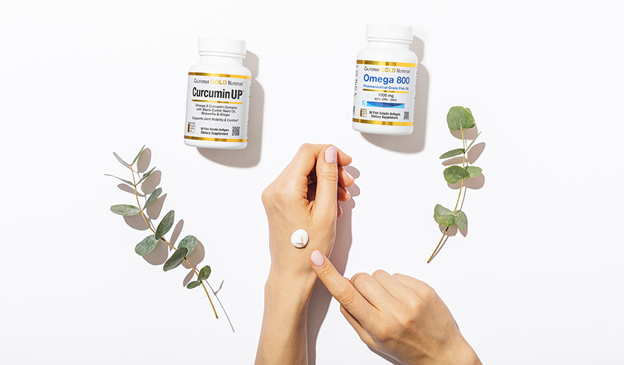 Overhead of applying lotion on hands with omega-3 and turmeric supplement bottles