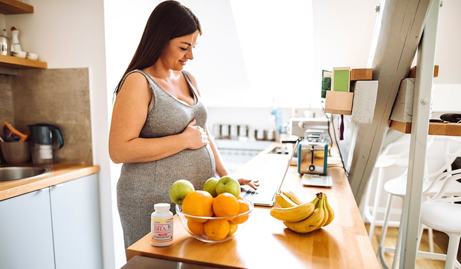 Pregnant woman eating healthy fruits in the kitchen