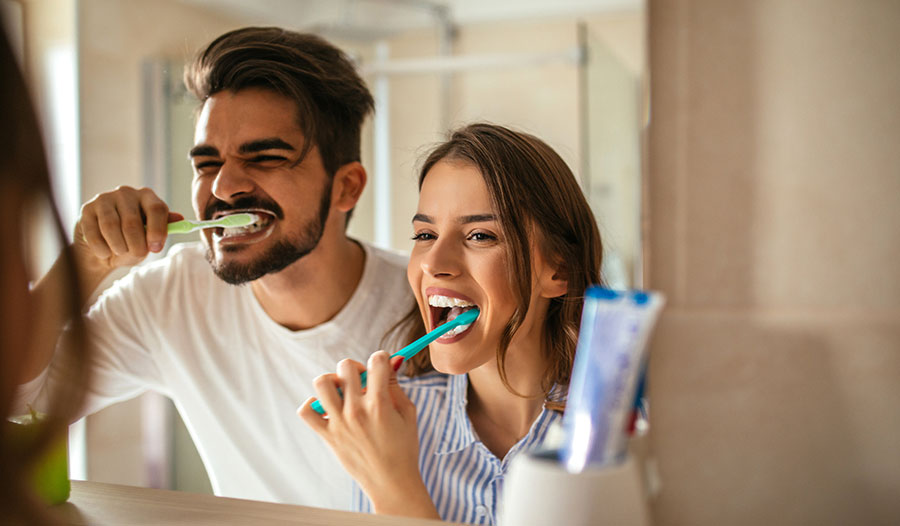 a couple brushing their teeth in the mirror based on their revamped oral care routine