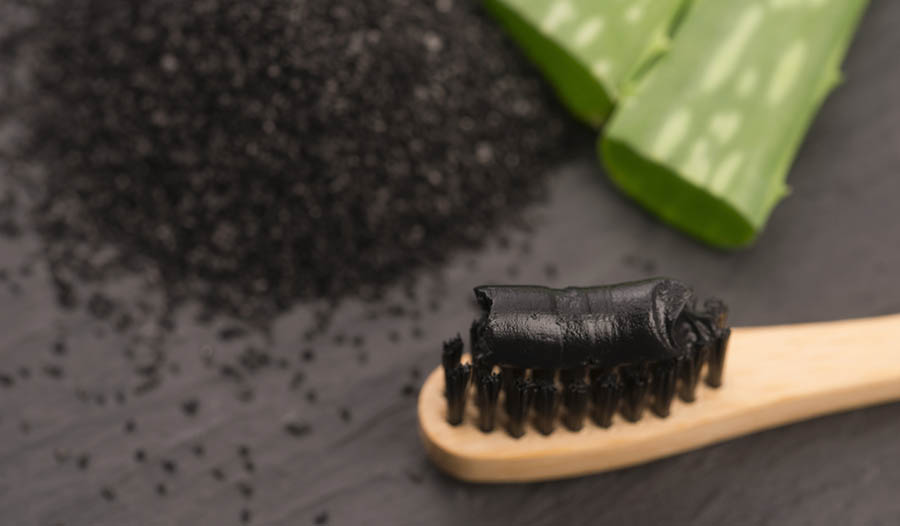 Charcoal toothbrush and toothpaste on black table to charcoal and aloe