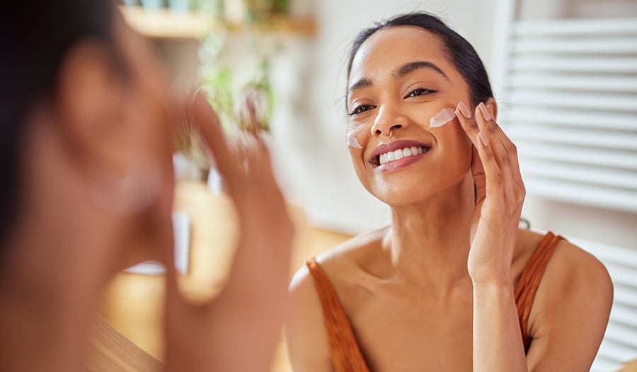 Woman applying skincare product to face looking in the mirror
