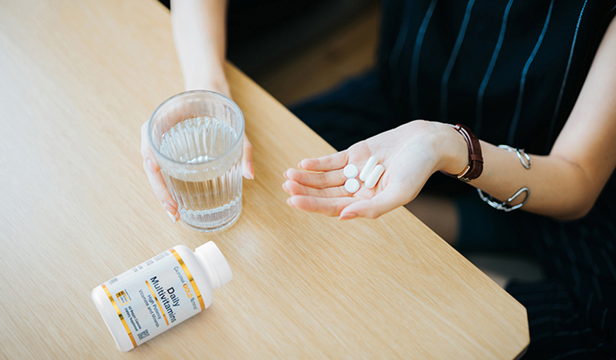 Woman taking vitamins and supplements with glass of water