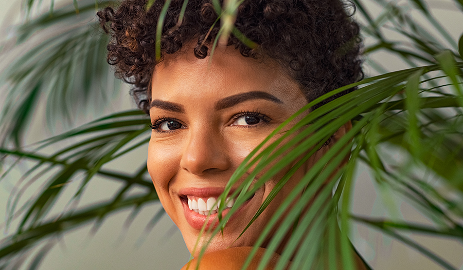 Young woman with curly short hair smiling through leaves