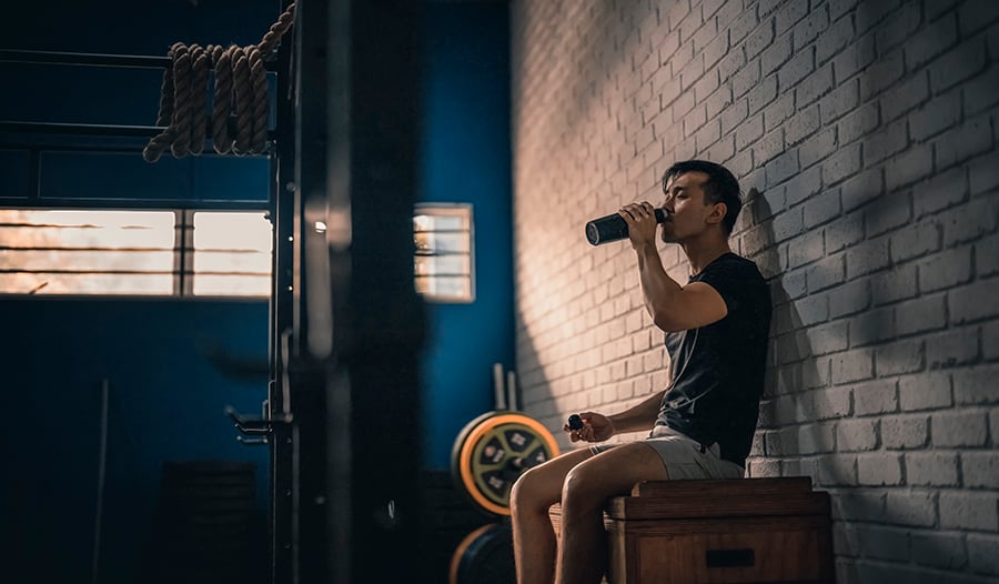 Asian male taking break from workout drinking water in gym