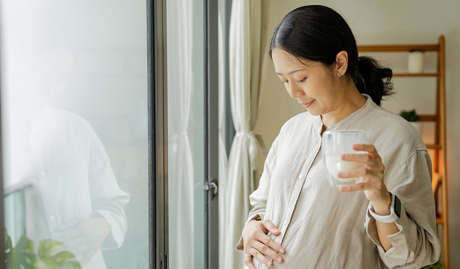 Pregnant asian woman holding belly at home by window