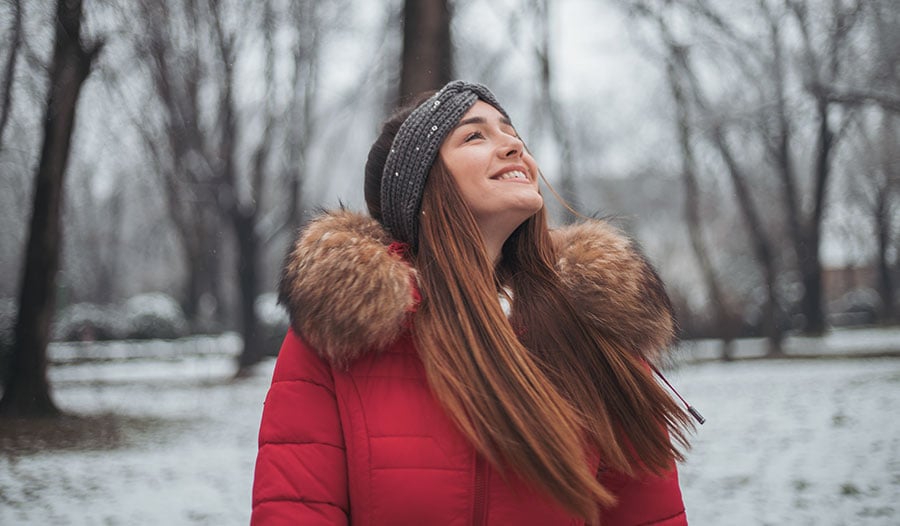 woman in red winter coat standing in the snow looking up at the sky