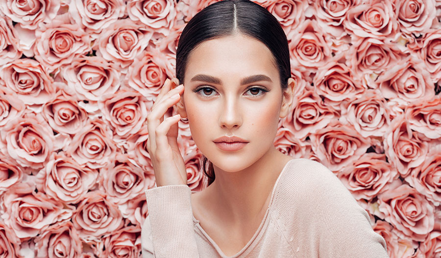 woman thinking about rose-infused beauty products in front of a wall of pink roses