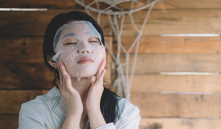 woman putting on sheet mask as part of her self care 