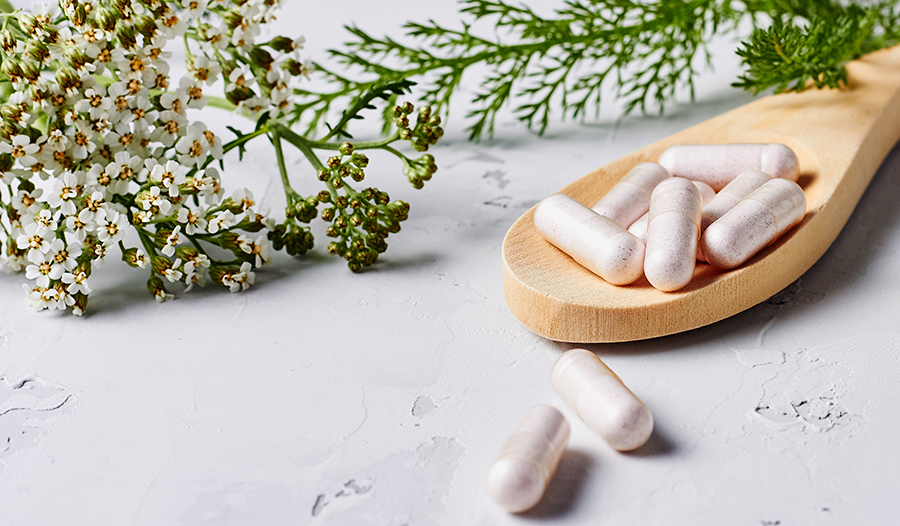 Herbal supplement in capsules and plants over grey background. 