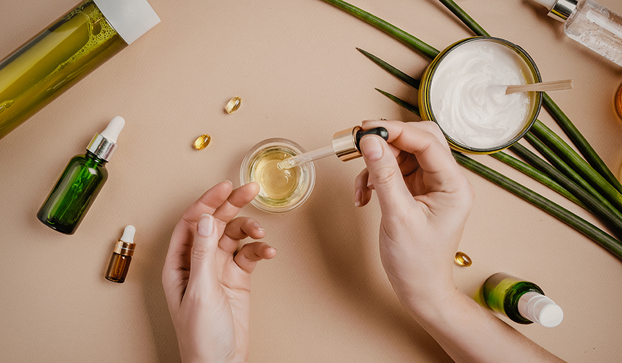 Women's hands with skincare products, serums, lotions, supplements on nude background with green fol