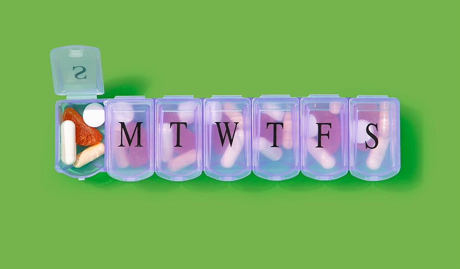 Supplements in daily pill box on green background