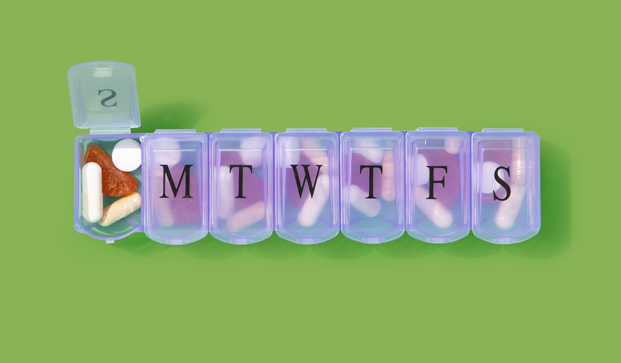 Supplements in daily pill box on green background