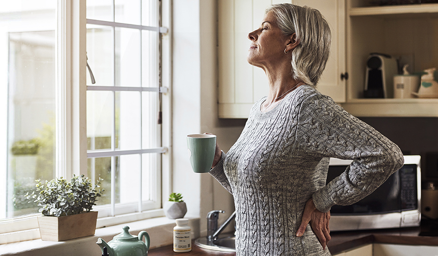 Woman standing near kitchen window with mug in her hand