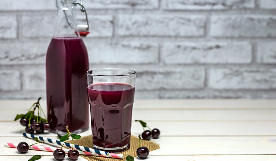 Tart cherry juice in glass and bottle with cherries and straws on table