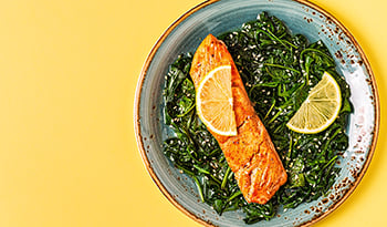 Grilled salmon with lemon on spinach on yellow table.