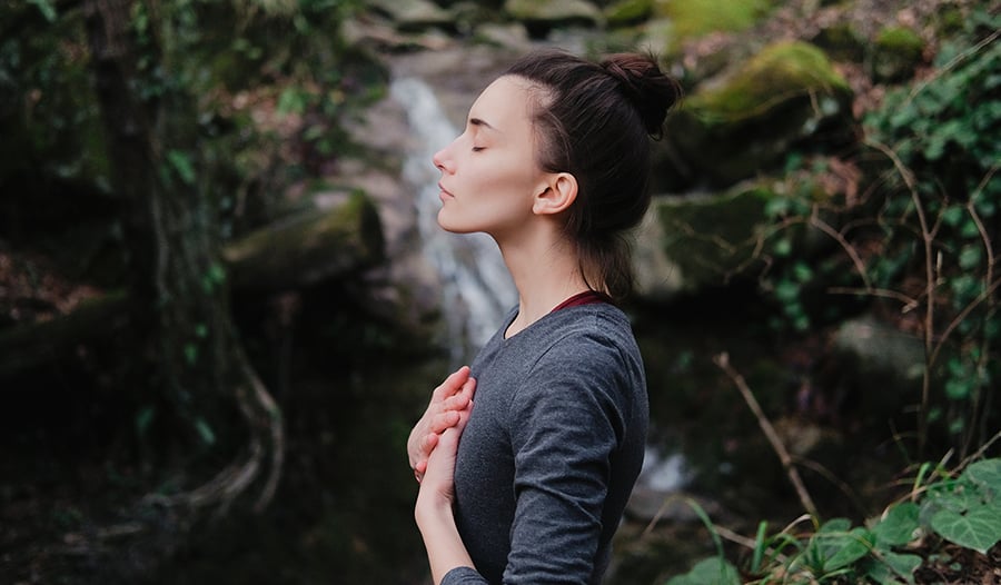 Young woman breathing deeply outdoors in front of waterfall