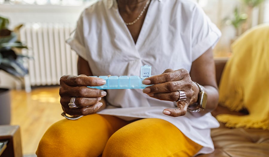 Elderly woman taking daily vitamins with pill organizer while sitting on couch